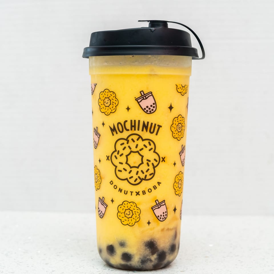Mochinut mango boba drink with black tapioca pearls and a black lid on a white background.