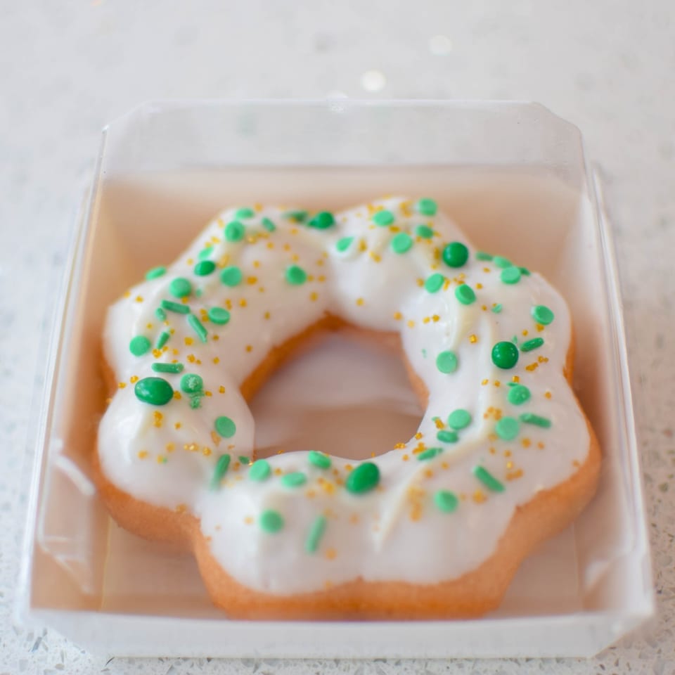 A star-shaped donut with white icing and green and gold sprinkles in a clear plastic container.