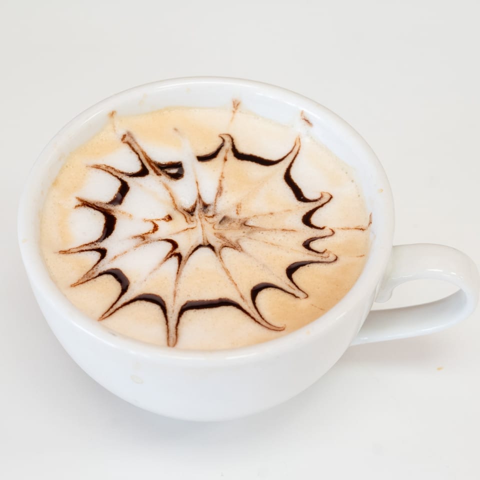 Close-up of a white cup of latte with intricate chocolate art on the foam.