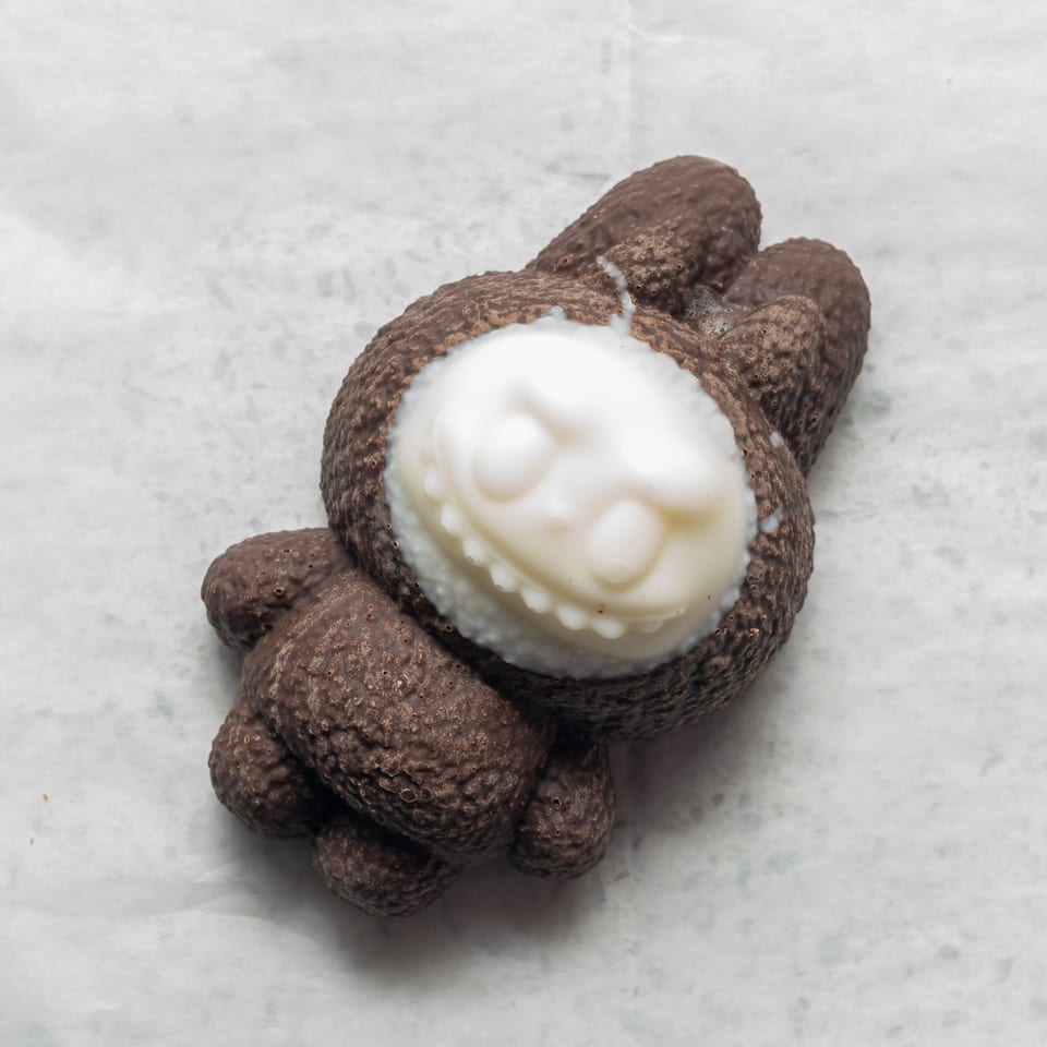 A chocolate bunny with a white chocolate face, detailed with eyes and a smile, on white parchment.