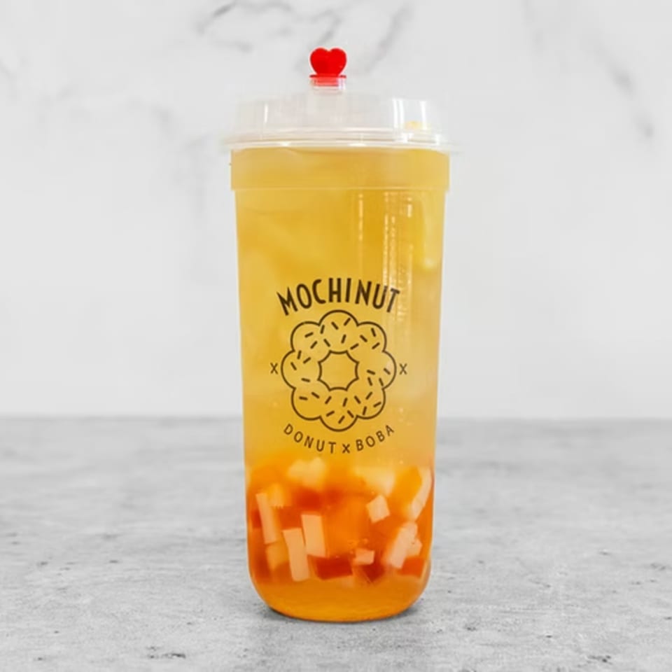 Mochinut boba tea with fruit pieces, a red heart stopper, and the brand logo.