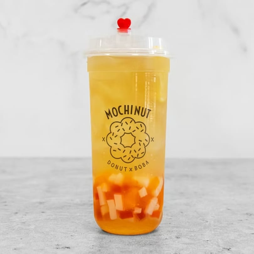 Mochinut boba tea with fruit pieces, a red heart stopper, and the brand logo.