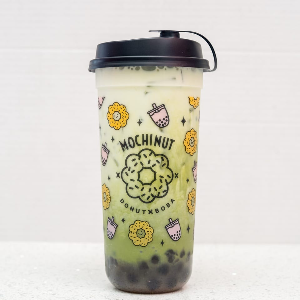 Mochinut matcha boba drink with a black lid, featuring a donut and boba cup pattern.