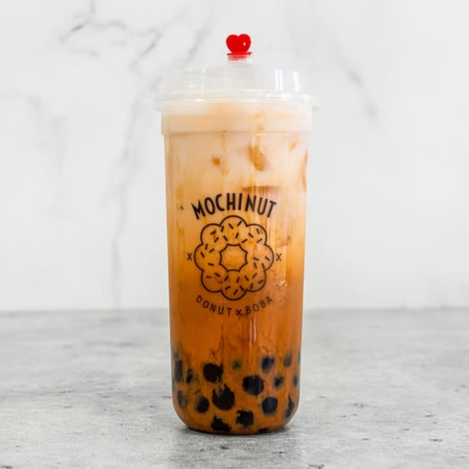Mochinut Thai tea with boba in a clear cup with a red heart stopper.