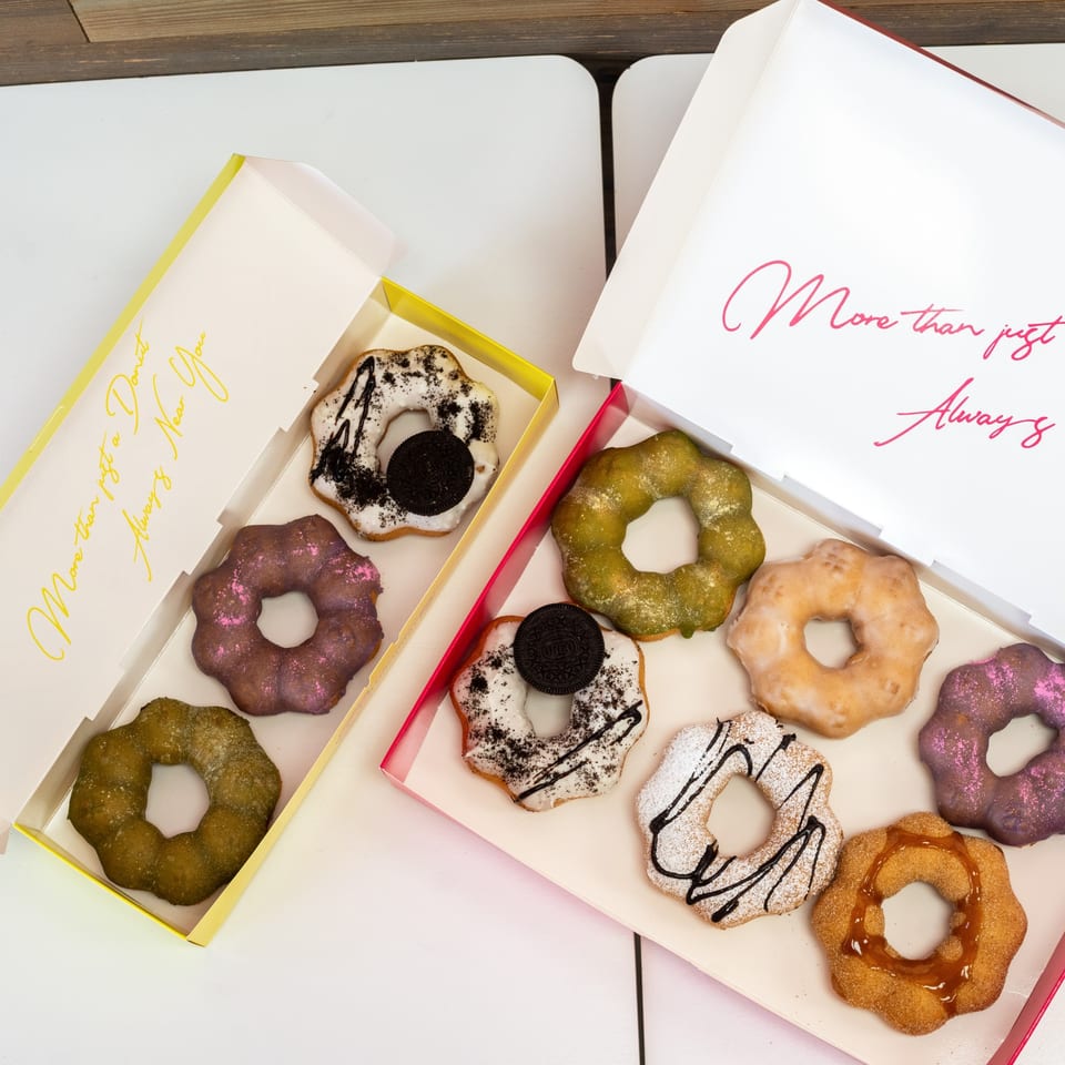 Two boxes of colorful mochi donuts with various toppings, including Oreo, matcha, and powdered sugar.