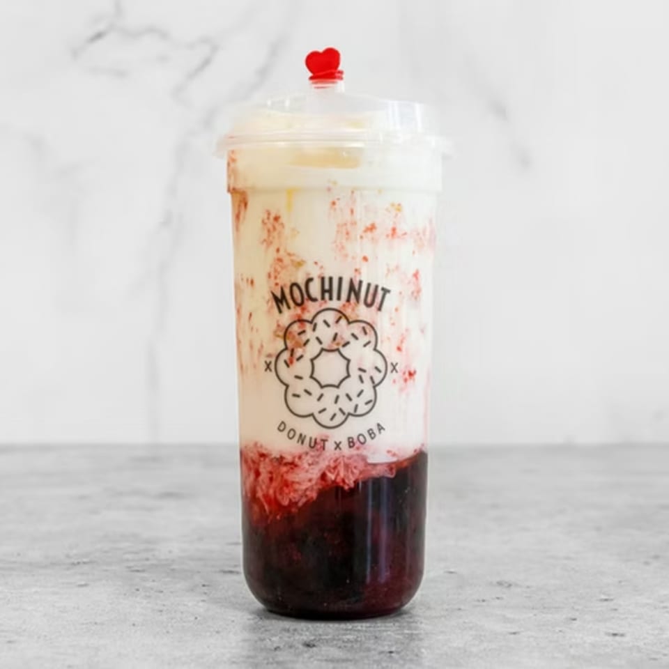 Mochinut strawberry boba drink with a red heart stopper on a white marble background.