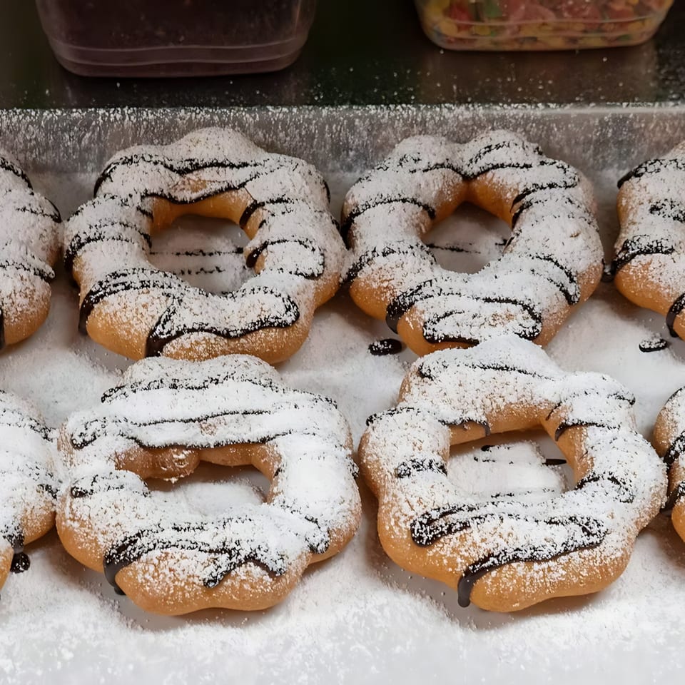 Rows of freshly baked churro donuts, drizzled with chocolate and dusted with powdered sugar.