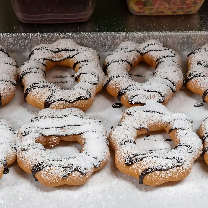 Rows of freshly baked churro donuts, drizzled with chocolate and dusted with powdered sugar.