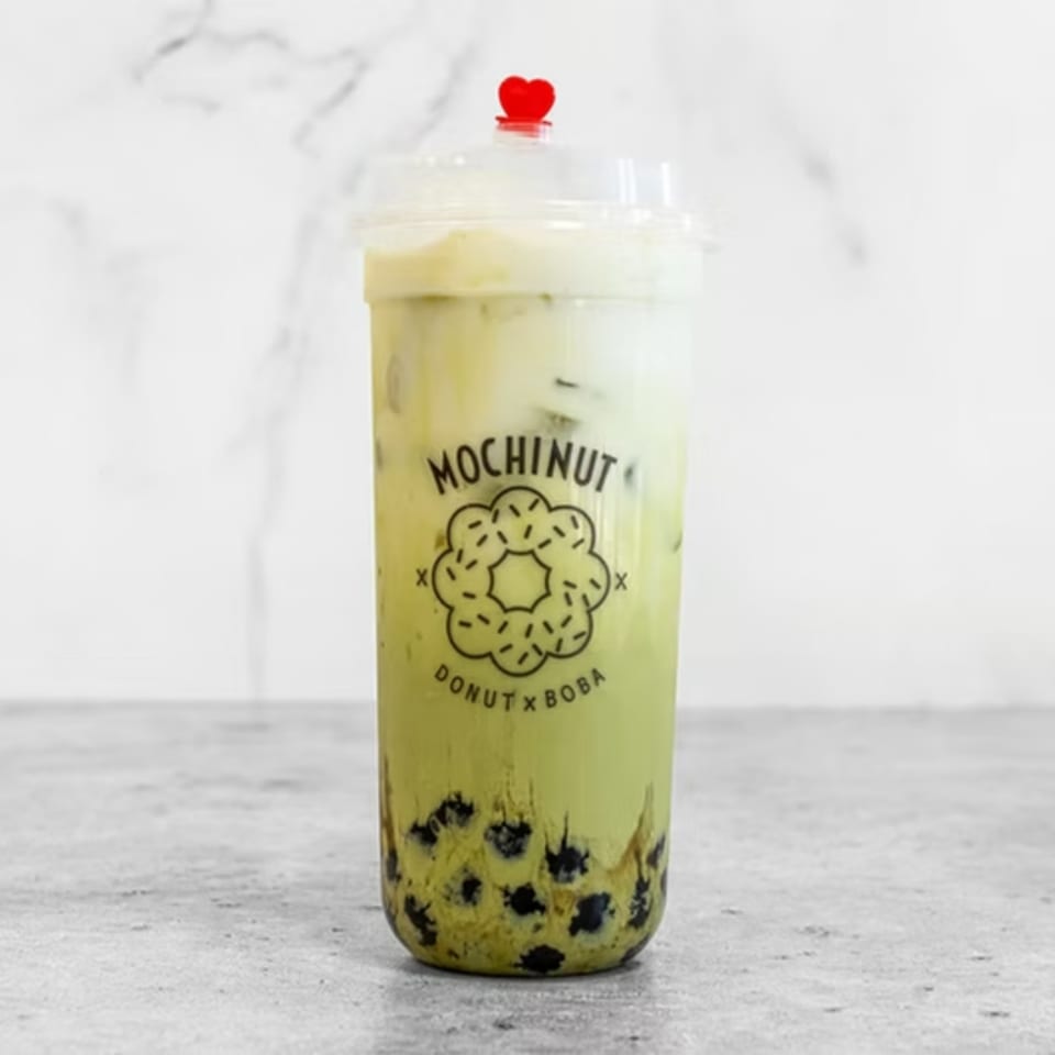 Mochinut matcha boba drink with a red heart stopper, on a white marble background.