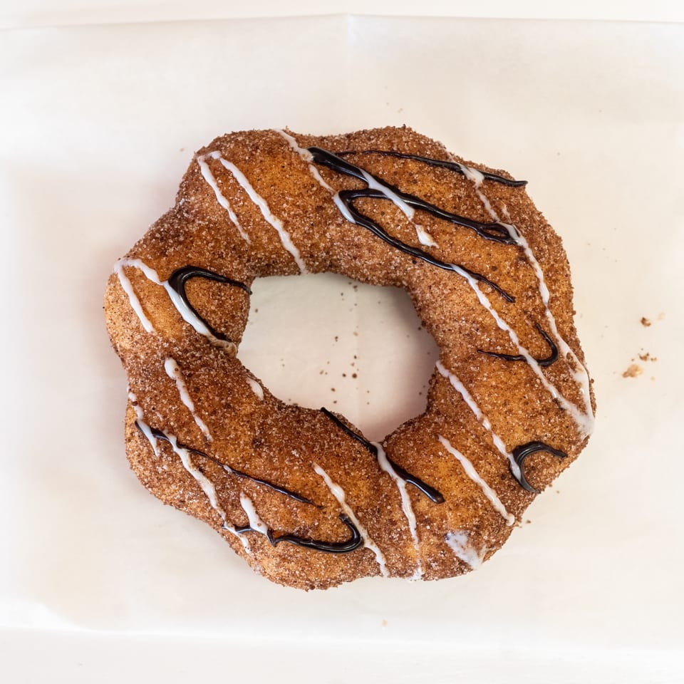 A cinnamon sugar churro donut with white and dark chocolate drizzle on a white background.