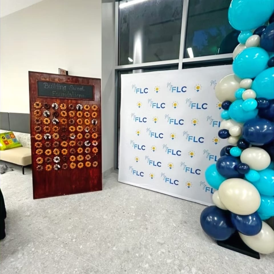 Event display featuring a “Building Sweet Foundations” board, FLC-branded backdrop, and blue, white, and teal balloon arrangement.