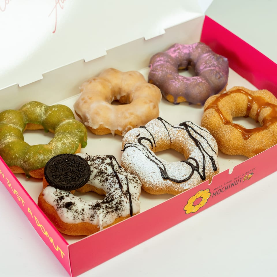 A pink MochiNut box filled with six colorful mochi donuts, including matcha, Oreo, and caramel flavors.