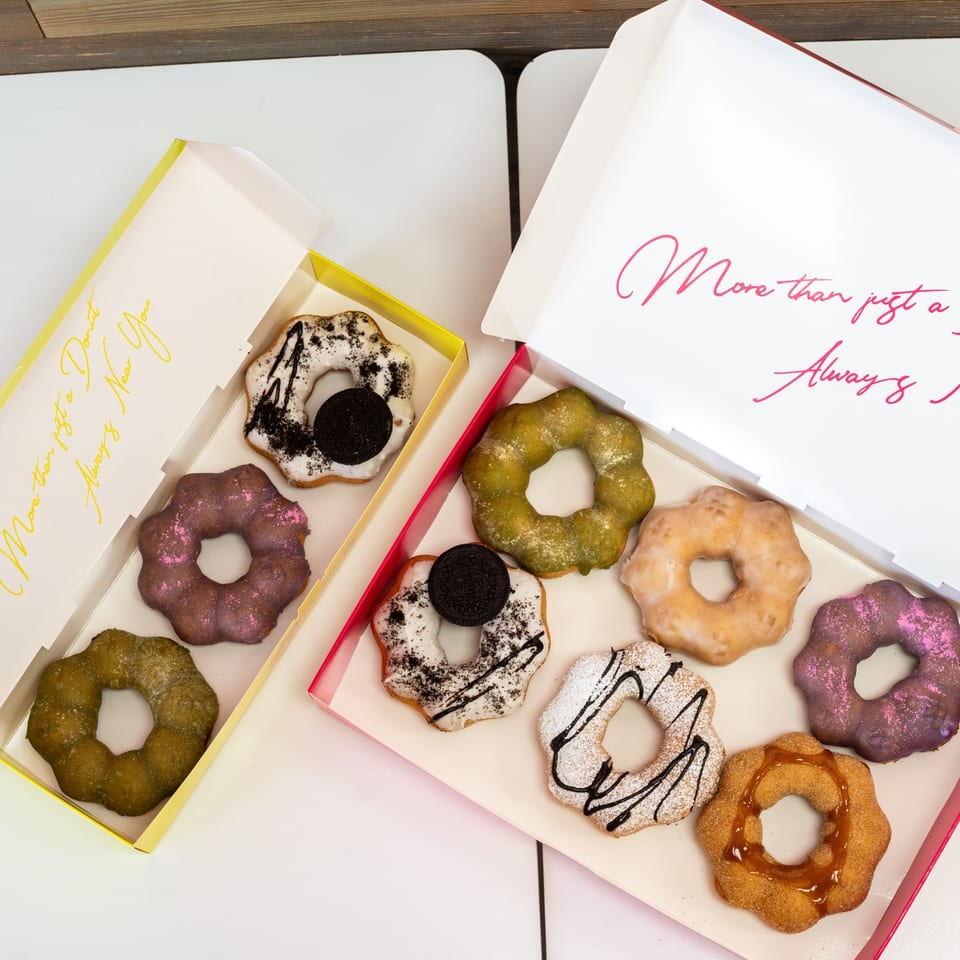 Two open boxes of colorful, uniquely shaped donuts with various toppings on a white table.