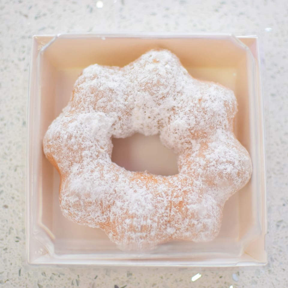 A star-shaped mochi donut, covered in powdered sugar, sits in a clear plastic container.